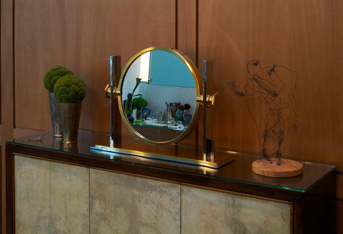 Custom bathroom vanity with wood paneling, round brass mirror, and sculptural accessories